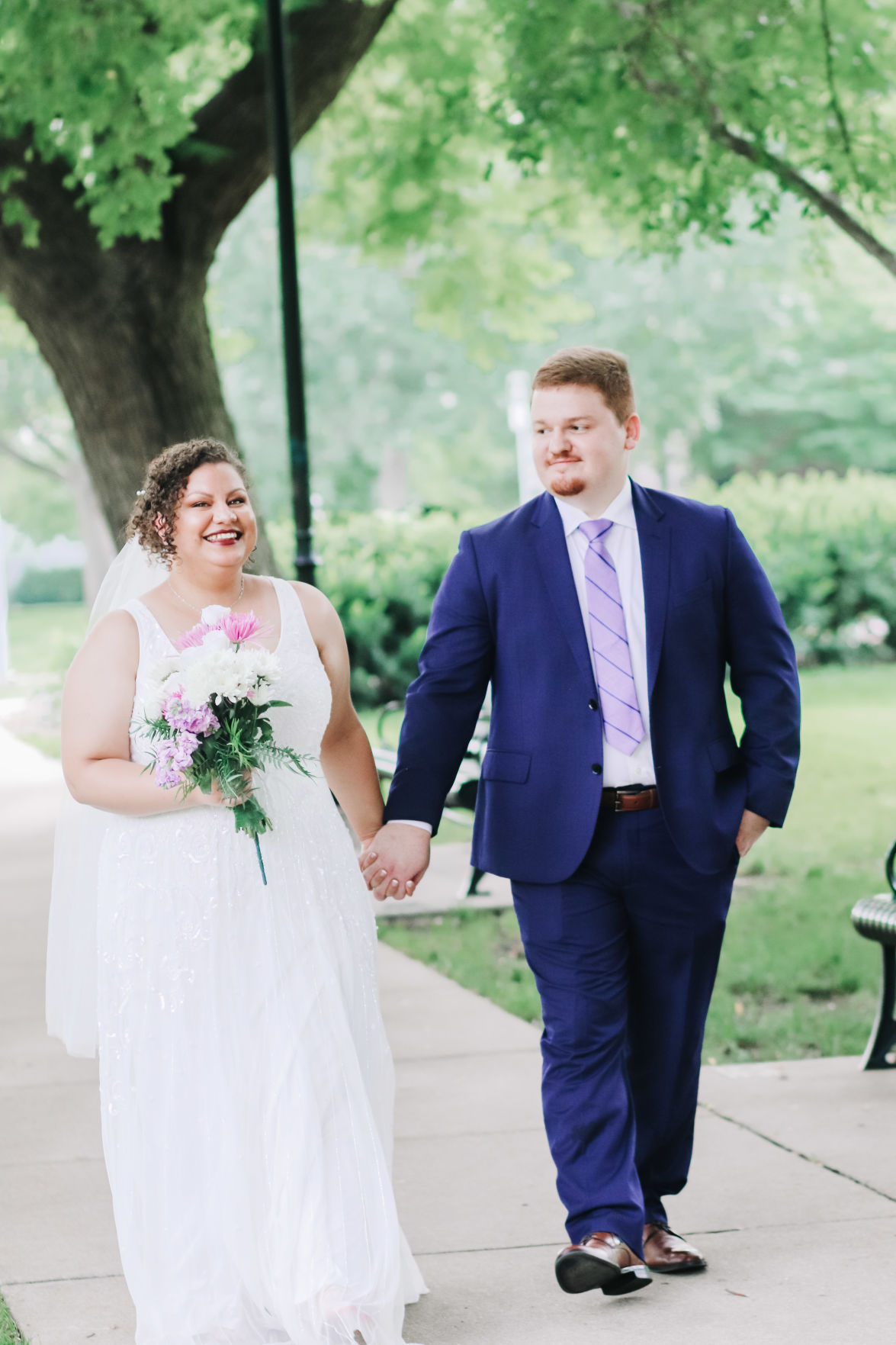 Justin and Rachel Thomas hold hands and walk down the sidewalk in their wedding apparel